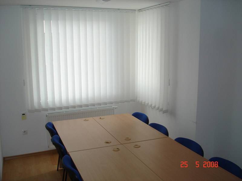 Gewerbeflächen mit Konferenztisch, blauen Stühlen und vertikalen Jalousien.