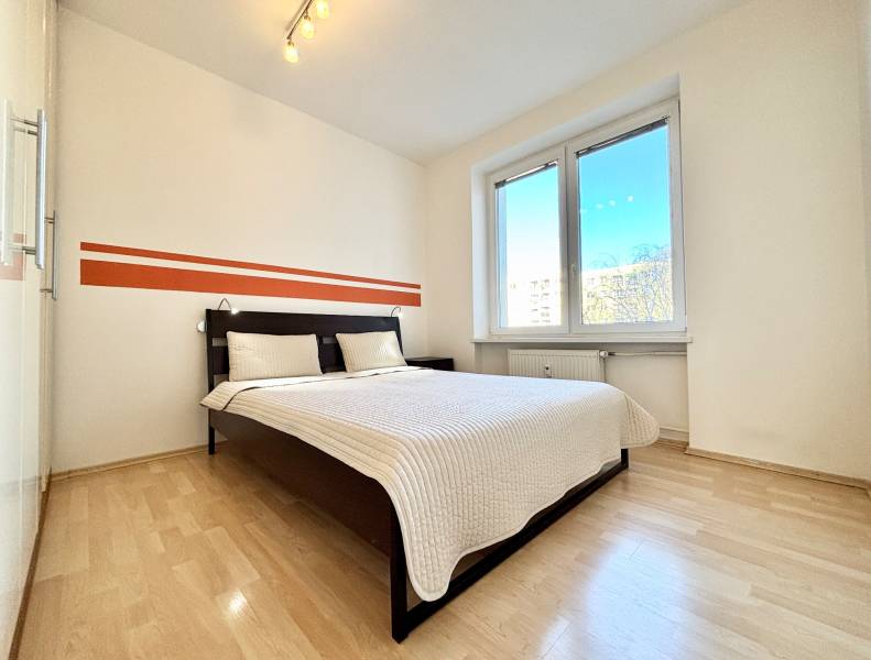 Schlafzimmer mit großem Bett, weißen Wänden und Boden in Holzoptik.