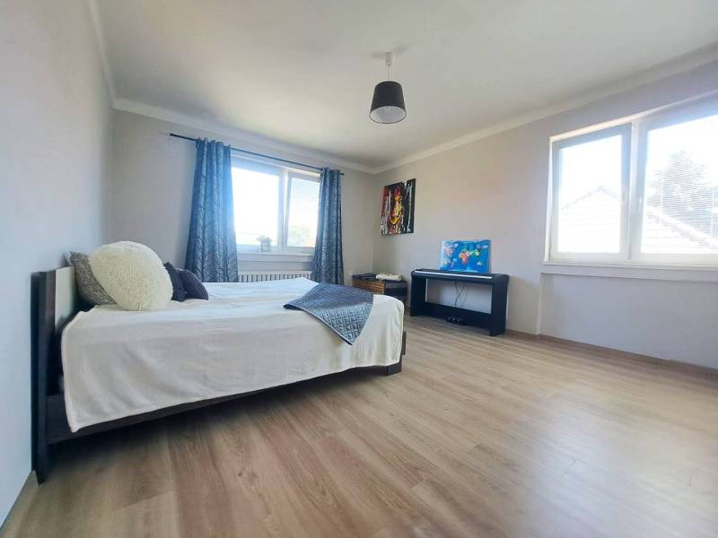 Ein Zimmer mit einem Bett, zwei Fenstern, einem Klavier und einem Boden mit Holzdekor in einem Einfamilienhaus.