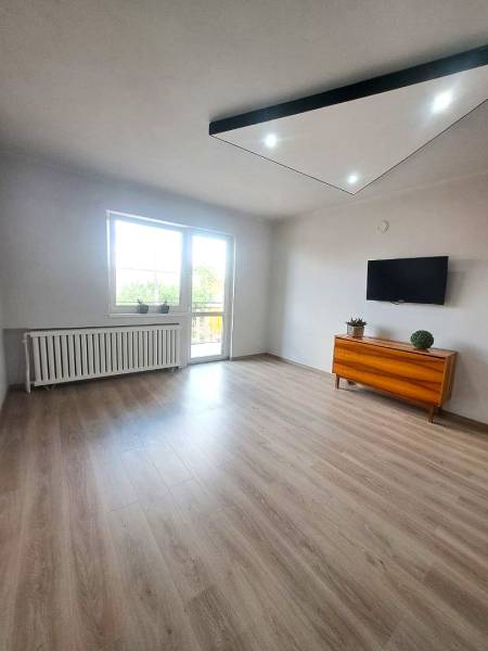 Wohnzimmer in einem Einfamilienhaus mit Holzboden, Fernseher und Kommode.