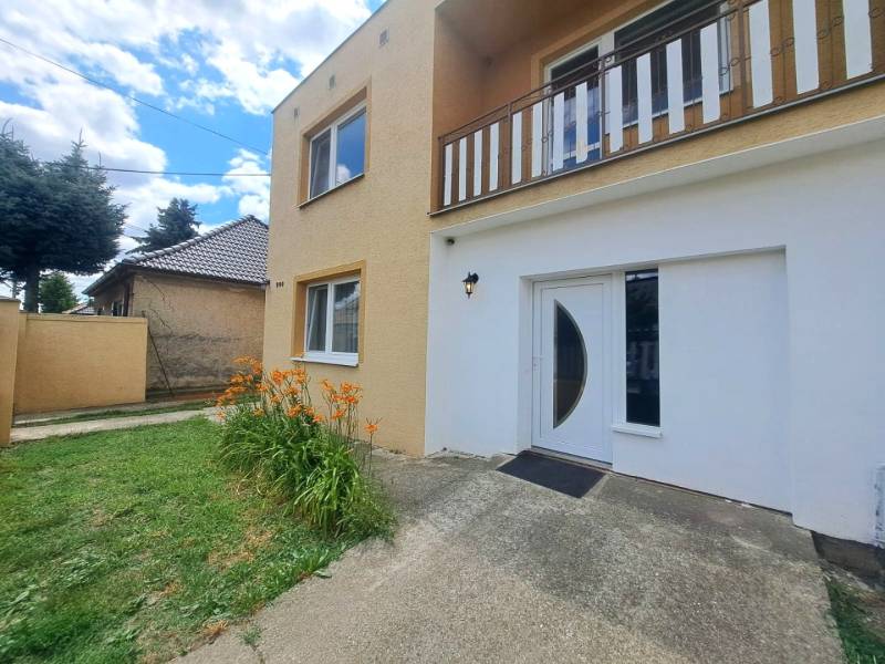 Ein Einfamilienhaus in Veľká Mača mit orangefarbenen Blumen, grünem Rasen und Eingangstüren.