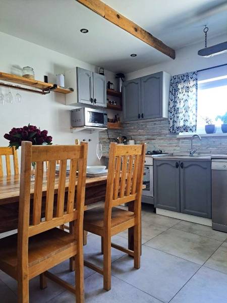 Küche in einem Einfamilienhaus mit Holztisch, Stühlen und grauen Schränken.