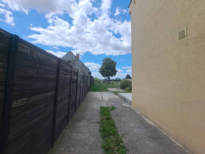 Ein Einfamilienhaus in Veľká Mača neben einem Holzzaun, eine Betonstraße, Wolken und ein Baum.