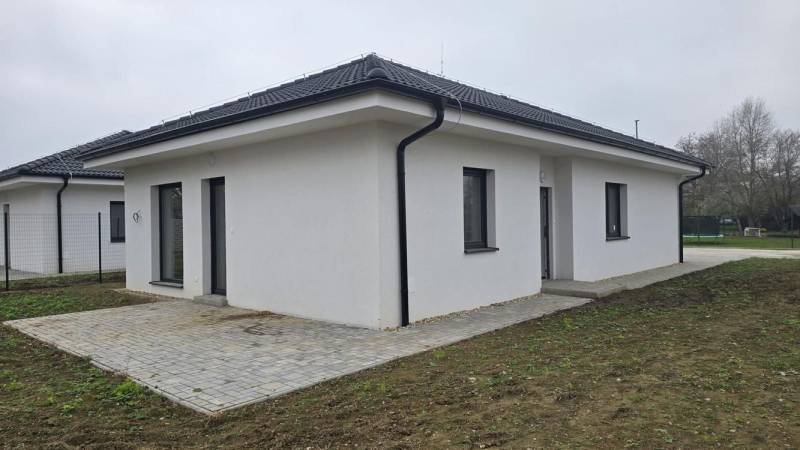 Ein Einfamilienhaus in Cífer mit einem Schrägdach und einer gepflasterten Terrasse im Garten.