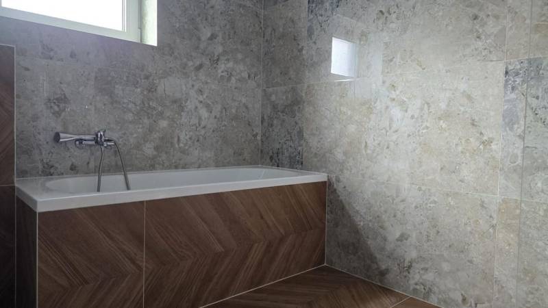 Badezimmer in einem Einfamilienhaus mit Badewanne, Fliesen mit Steinmuster, Boden mit Holzdekor.