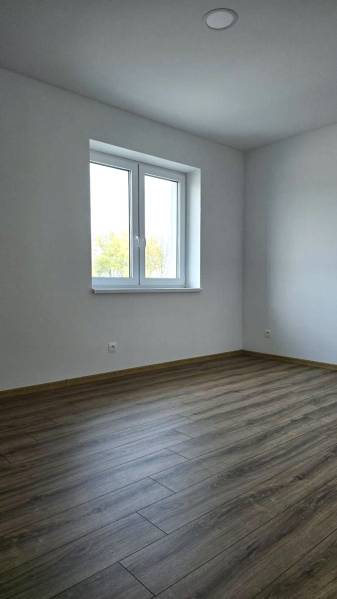 Ein Zimmer in einem Einfamilienhaus mit einem Boden in Holzoptik und weißen Wänden.