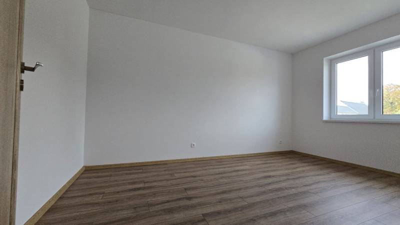 Ein Zimmer in einem Einfamilienhaus mit einem Boden in Holzoptik und einem großen Fenster.