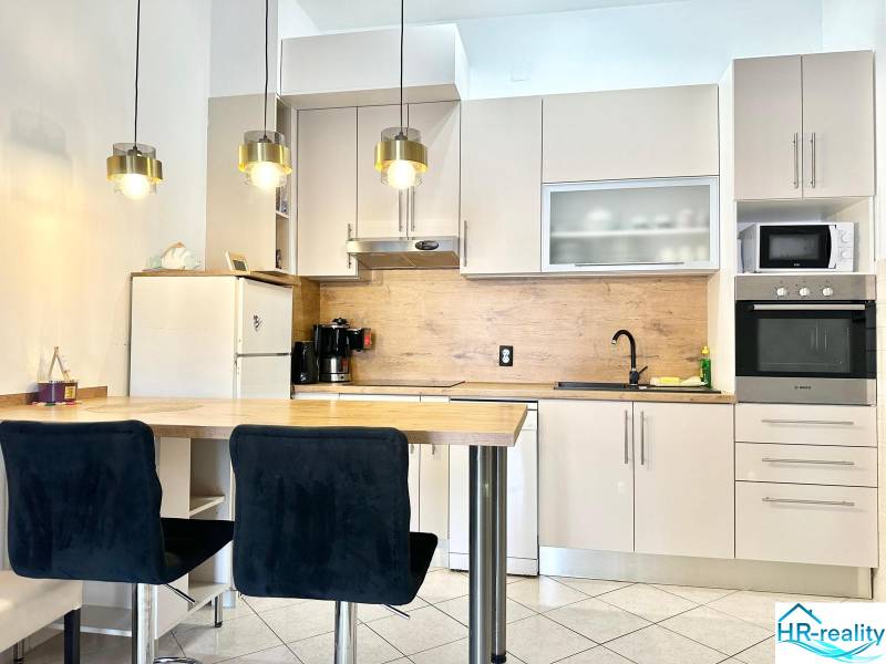 Küche in einer Ferienwohnung mit Bartresen, Hängeleuchten und weißem Schrank.