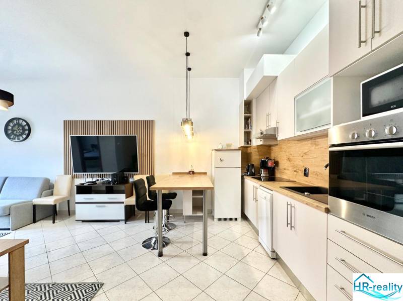 Innenraum eines Ferienapartments mit Küchenzeile, Esstisch und Fernseher an der Wand.