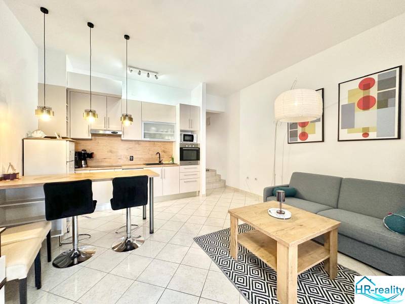 Ferienwohnung mit Kochnische, Esstisch, Sofa und Kunstgemälden an der Wand.