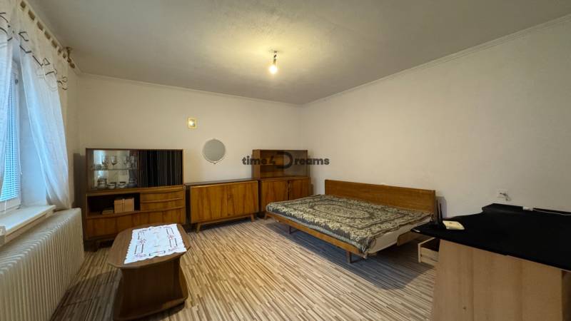 Schlafzimmer mit Möbeln im Retro-Stil, Boden mit Holzdekor, großes Fenster mit Heizkörper.