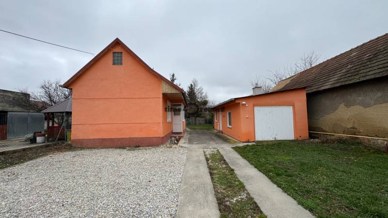 Ein Einfamilienhaus in Čechynce mit einer orangefarbenen Fassade, einem Betonweg und einer Garage.