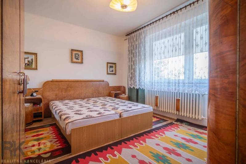 Schlafzimmer in einem Einfamilienhaus mit Bett, Teppichen und Vorhängen am Fenster.