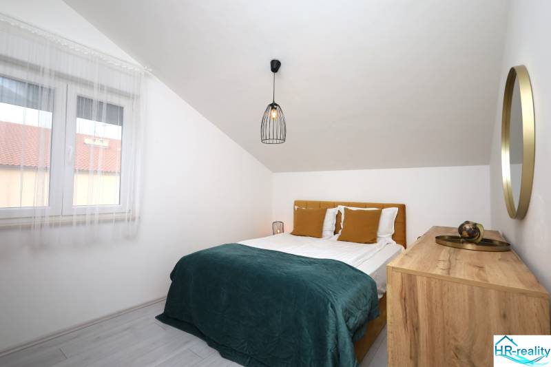 Schlafzimmer im Ferienapartment mit Doppelbett, Fenster und Kommode unter dem schrägen Dach.