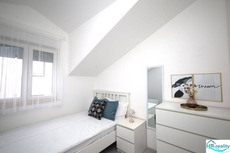 Helles Schlafzimmer in einer Ferienwohnung mit Bett, Nachttisch und Kommode.