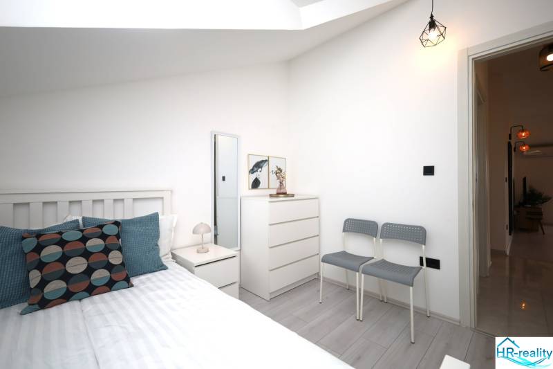 Ferienwohnung mit hellem Schlafzimmer, Bett, Kommode und Kissen, Boden mit Holzdekor.