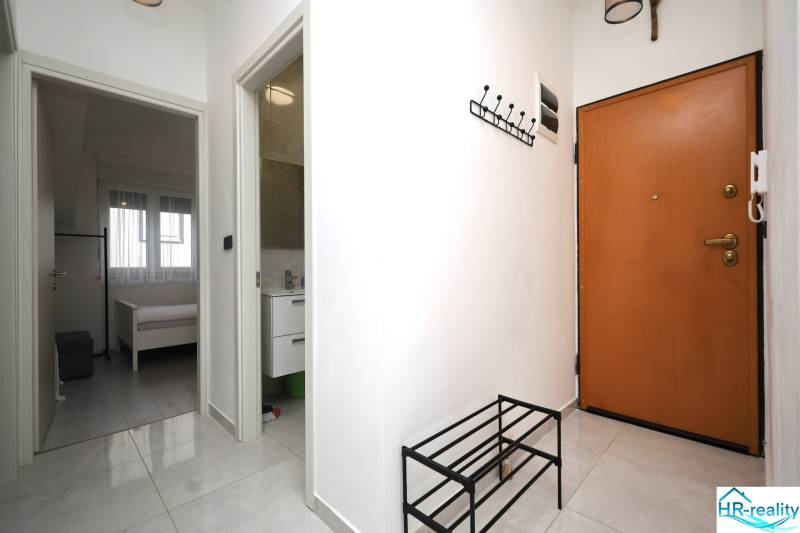 Ferienwohnung mit Fliesenboden, Garderobe, offenen Türen zum Schlafzimmer und Badezimmer.