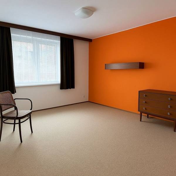 Ein Zimmer mit einer orangefarbenen Wand, Möbeln, einem Fenster und einem Teppichboden in einem Einfamilienhaus.