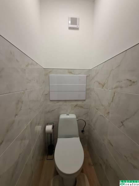 Toilette in einem Einzimmerapartment mit einem Boden in Holzoptik und Fliesen, die Marmor imitieren.