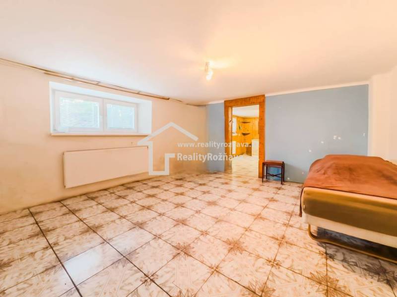 Ein Zimmer mit Fliesen in einem Einfamilienhaus, ein Bett an der Wand, ein Fenster mit Heizkörper.