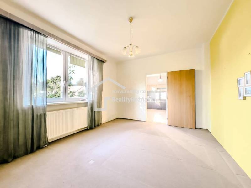 Ein Zimmer mit einem großen Fenster, einem Heizkörper und einem Durchgang in einem Einfamilienhaus.