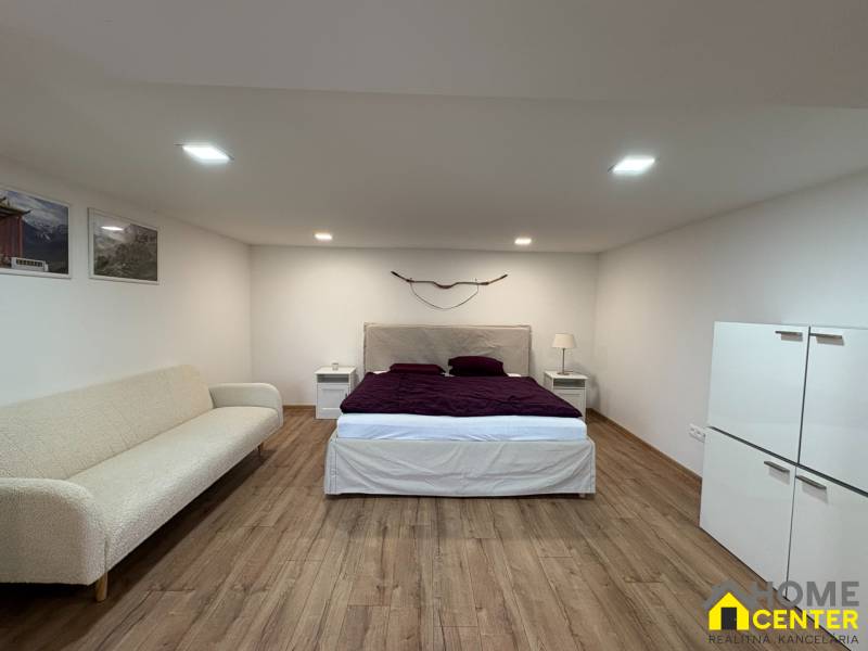 Innenraum einer Einzimmerwohnung mit Bett, Sofa und Holzboden.