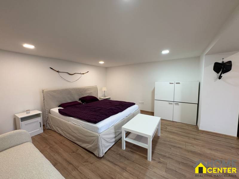 Schlafzimmer in einer Einzimmerwohnung mit Holzboden und einem Bett mit violetter Tagesdecke.