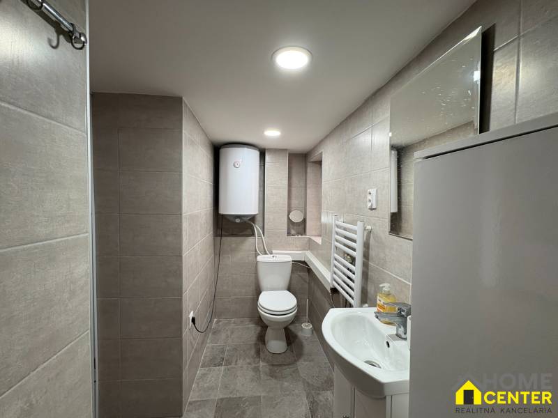 Badezimmer in einer Einzimmerwohnung mit Duschkabine, Waschbecken und WC, Fliesen an den Wänden.