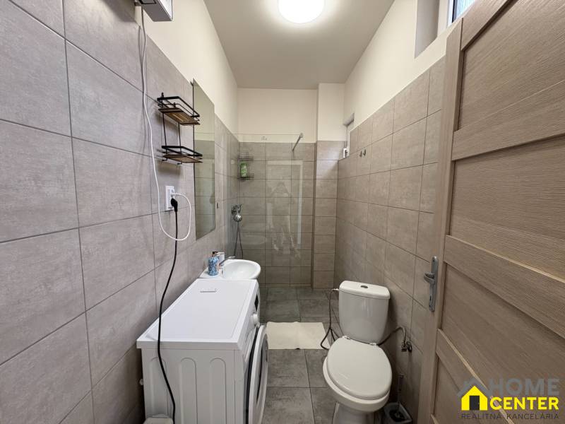 Badezimmer in einer Einzimmerwohnung mit Waschmaschine, Waschbecken und Duschkabine in neutralen Farbtönen.