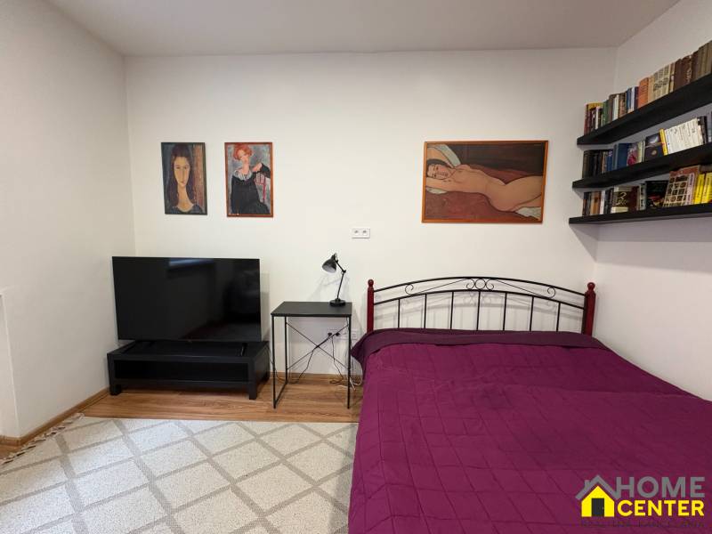 Schlafzimmer in einer Einzimmerwohnung mit Fernseher und Bildern an den schlichten Wänden.