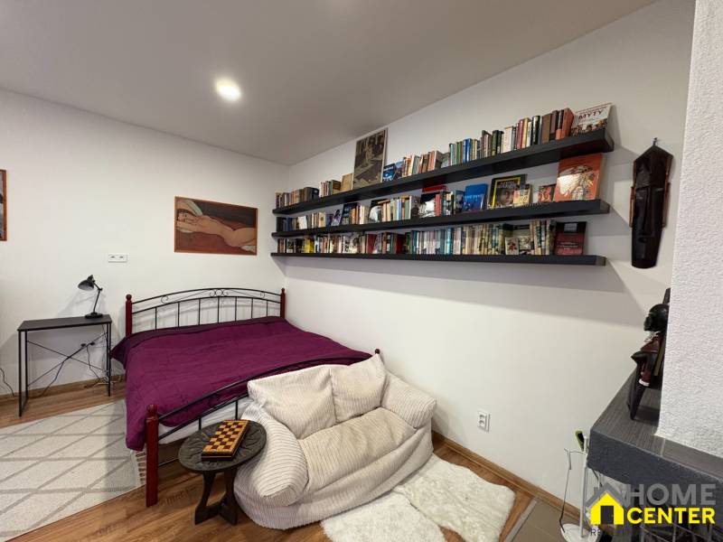 Schlafzimmer in einer Einzimmerwohnung mit Bett, Bücherregal und Holzboden.