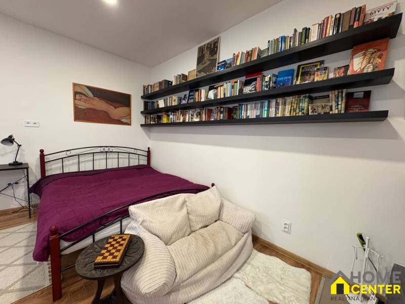 Einzimmerwohnung mit Bibliothek, Kunst an der Wand und einem Bett mit purpurner Tagesdecke.