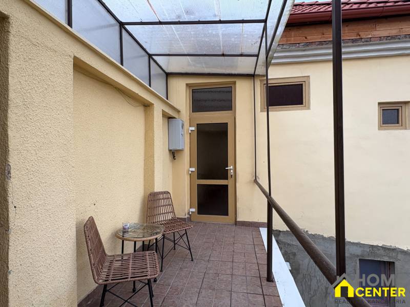 Überdachte Terrasse mit zwei Stühlen und einem Tisch vor dem Eingang zu einem Einzimmerapartment.