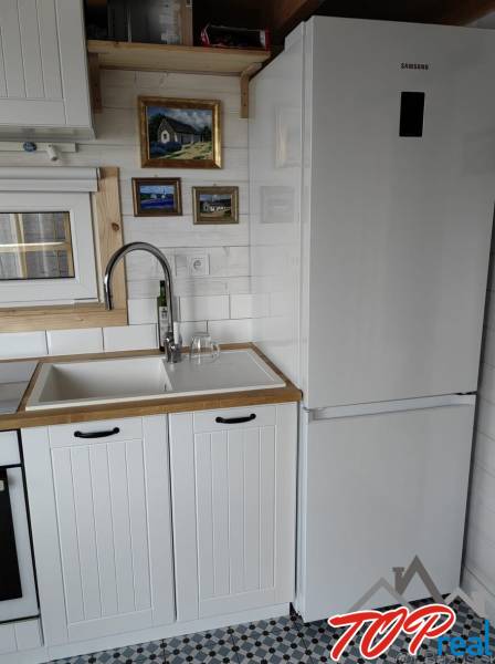 Küche im Einfamilienhaus mit weißer Küchenzeile, Kühlschrank und Kunstbildern an der Wand.