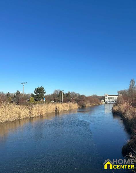 Ein Fluss umgeben von Schilf in den Gärten der Neuen Siedlung in Komárno unter blauem Himmel.