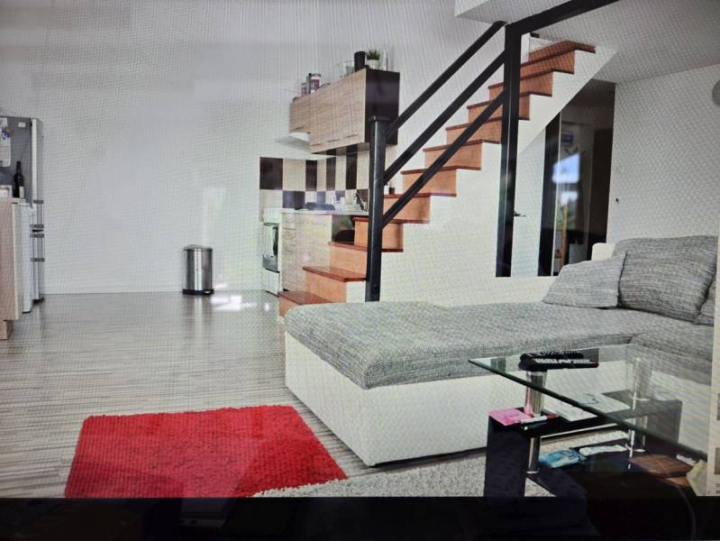 Wohnzimmer mit Küchenzeile, Treppe, Sofa, Glastisch und Holzboden.