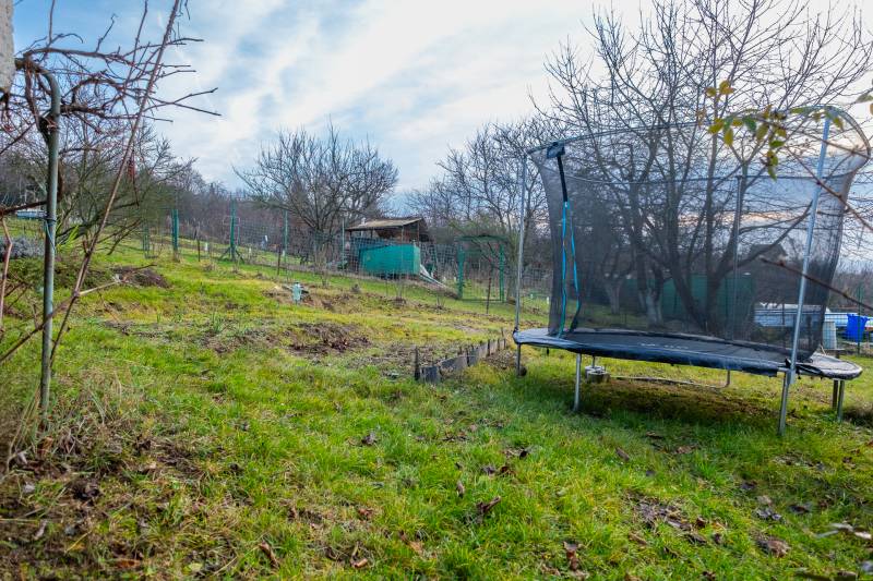 Trampolin und Gartenhaus in einem Garten in Prešov, umgeben von Bäumen und Gras.