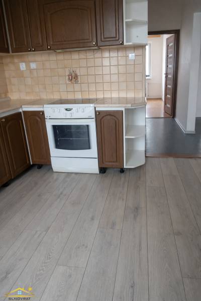 Küche mit braunen Schränken, weißem Herd und Bodenbelag in Holzoptik, in einer 3-Zimmer-Wohnung.