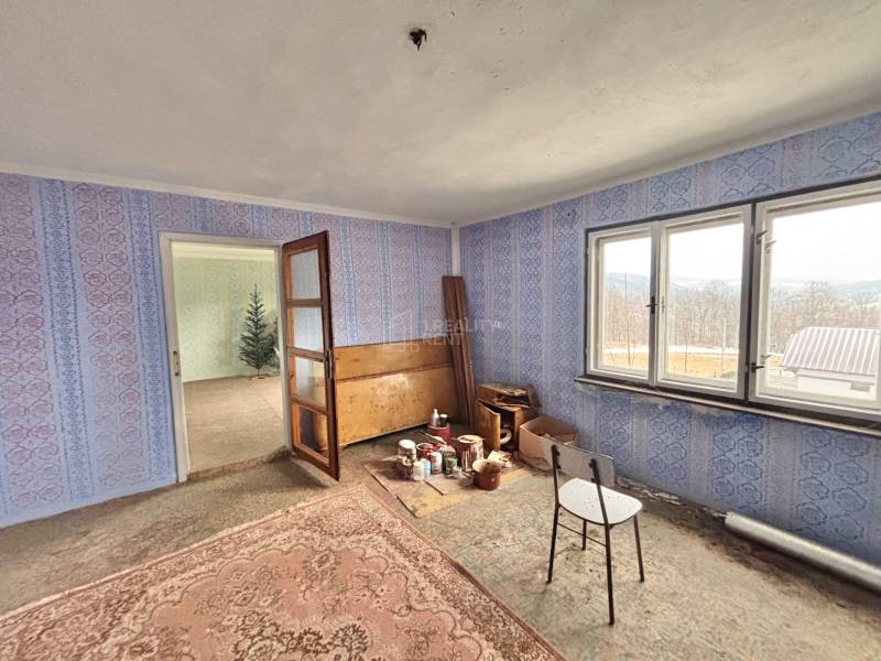 Ein Zimmer in einem Einfamilienhaus mit blauer Tapete, alten Möbeln und einem Teppich.