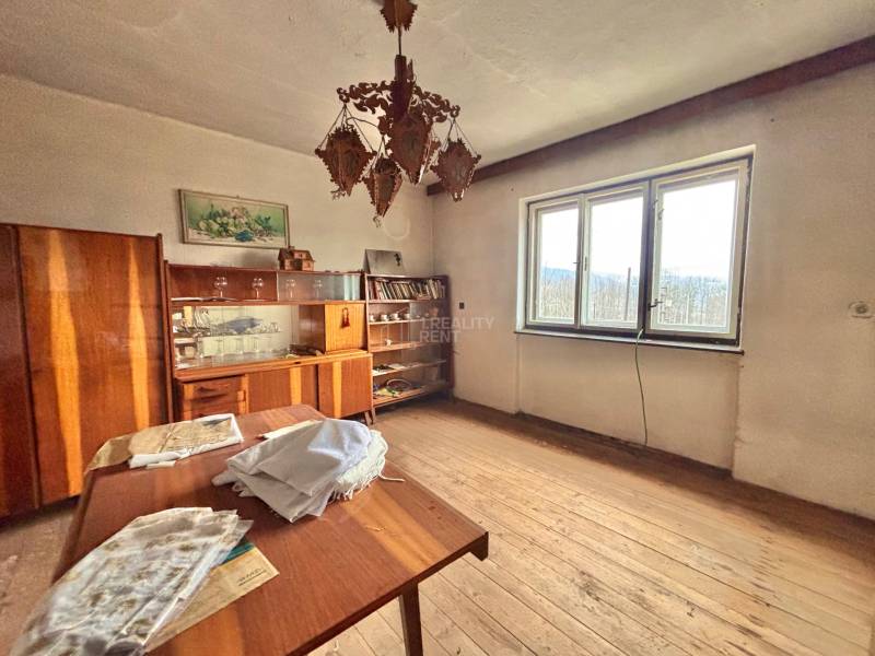 Ein Zimmer in einem Einfamilienhaus mit Holzelementen, Vintage-Möbeln, einem Kronleuchter und einem großen Fenster.