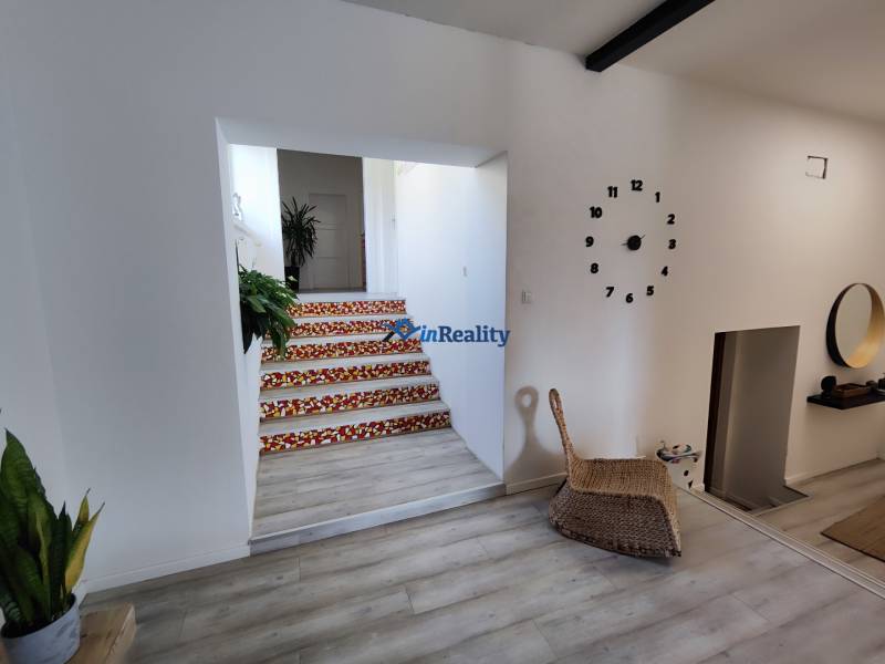 Innenraum eines Einfamilienhauses mit einer Uhr an der Wand, einem Boden in Holzoptik und Treppen mit buntem Muster.