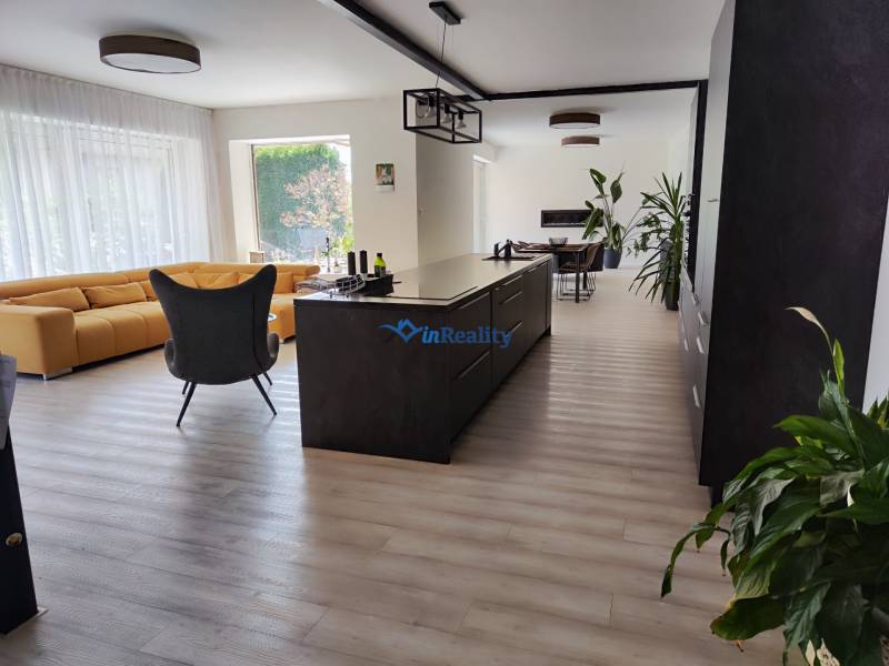 Küche und Wohnzimmer im Einfamilienhaus mit Insel, gelbem Sofa und Boden in Holzoptik.