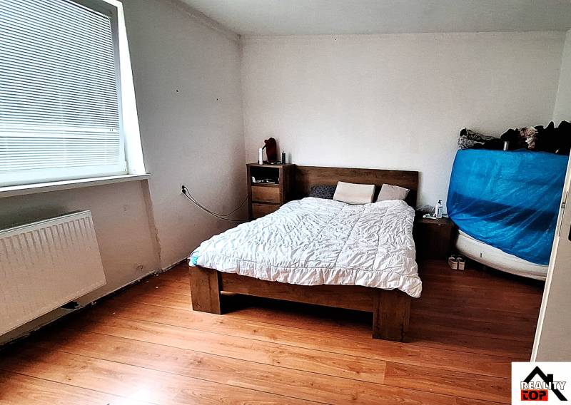 Schlafzimmer im Einfamilienhaus mit Bett, Kommode und Boden mit Holzdekor.