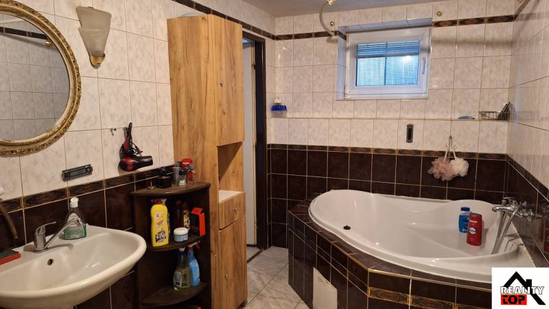 Ein Badezimmer mit einer Eckbadewanne, einem weißen Waschbecken und Holzmöbeln in einem Einfamilienhaus.