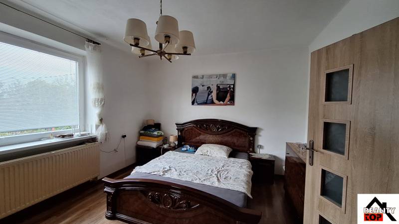 Schlafzimmer in einem Einfamilienhaus mit Bett, Kronleuchter und Boden in Holzoptik.