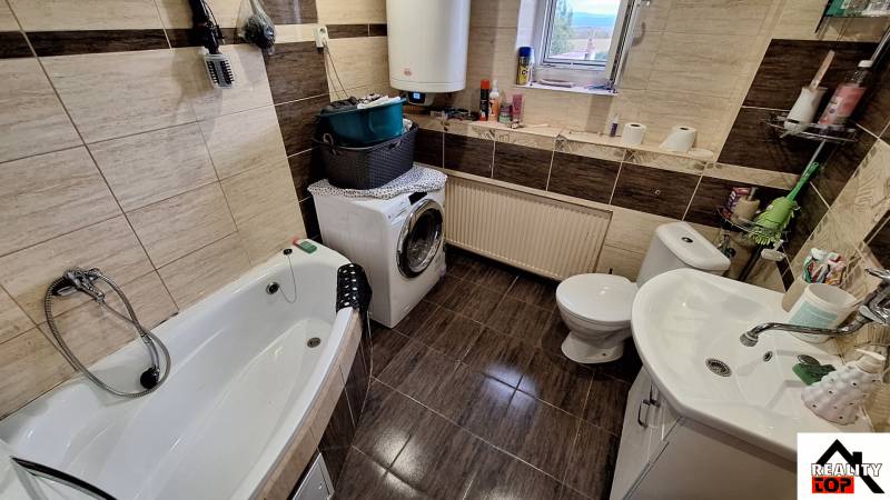 Badezimmer in einem Einfamilienhaus mit Badewanne, Waschmaschine und dekorativen braunen Fliesen.