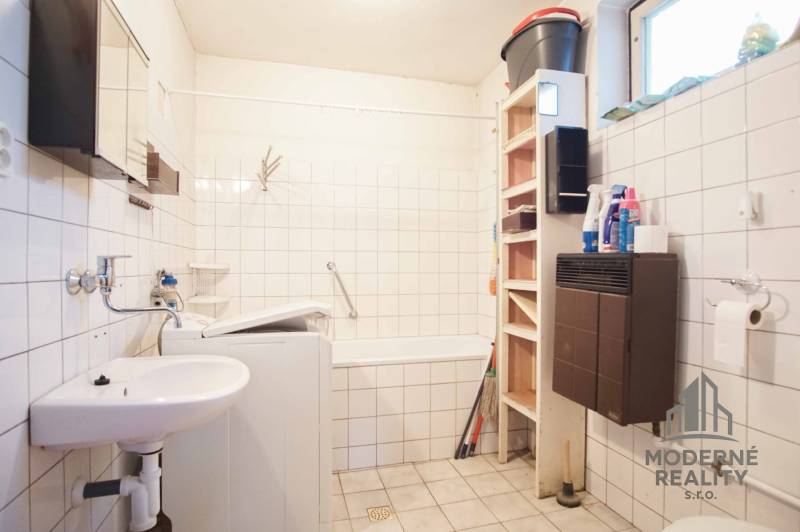 Badezimmer in einem Einfamilienhaus mit Badewanne, Waschbecken, Waschmaschine und Regalspeicher.