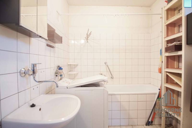 Ein Badezimmer in einem Einfamilienhaus mit einer Badewanne, einem Waschbecken und einer Waschmaschine, weiße Fliesen.