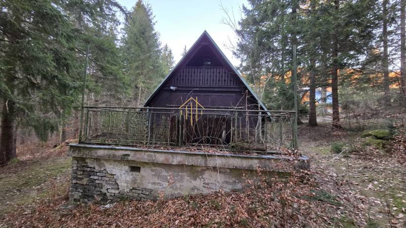 Eine Holzhütte umgeben von Bäumen in der Straße Krpáčovo in Krpáčovo bei Einbruch der Dämmerung.
