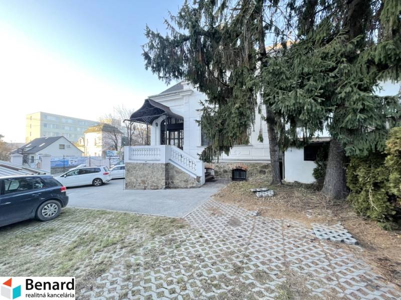 Das Gebäude in der Vajanského-Straße in Prešov mit Zufahrtsstraße, Autos und Tannen im Vordergrund.